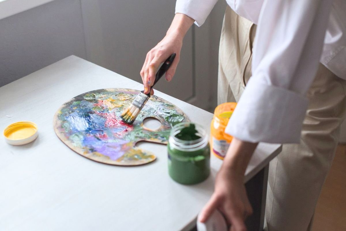 Person holding a paintbrush and mixing colours on an artist's palette while enjoying a creative hobby in retirement.