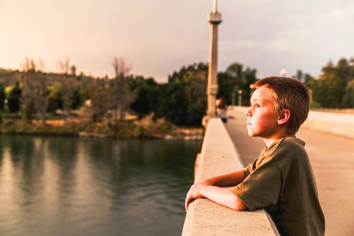 Young boy standing on a bridge looking thoughtfully across the water, reflecting the hidden emotions behind child behaviour.