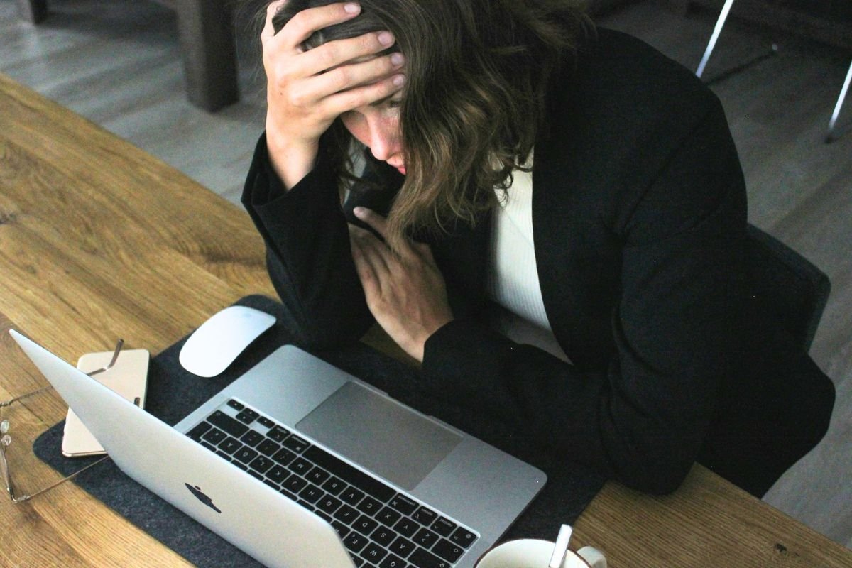 Overwhelmed woman sitting at a laptop with her head in her hands, reflecting emotional exhaustion caused by family pressure and people pleasing.