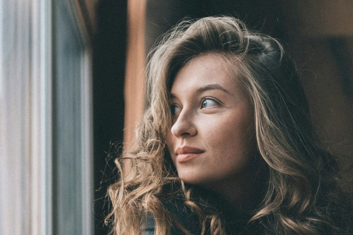Composed woman sitting beside a window with a gentle smile