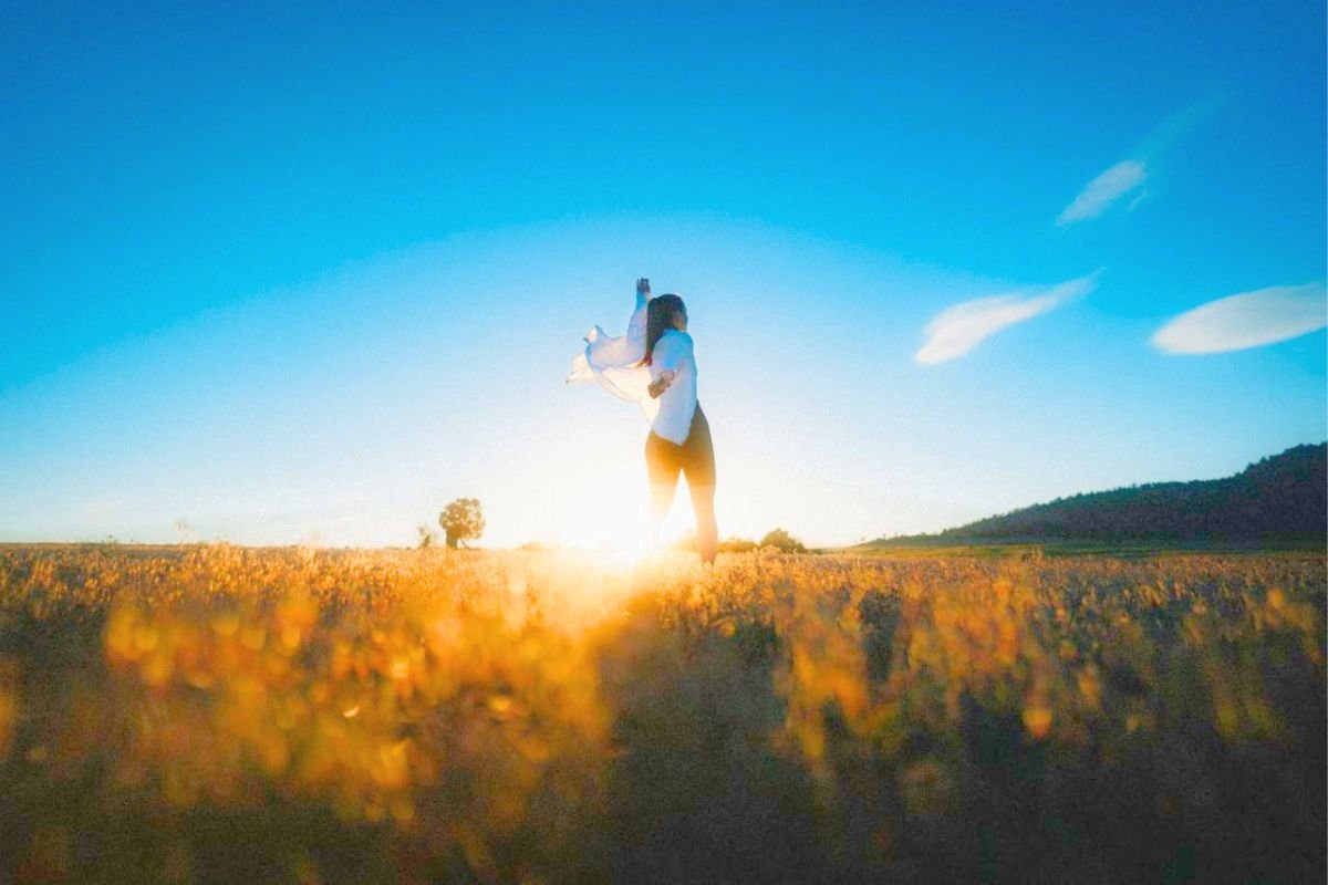 Woman walking towards the sunrise across open grassland, representing self respect, healthy boundaries, and moving forward with confidence and hope.